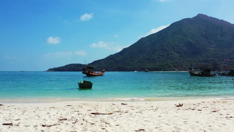 barcos de pesca flotando en un puerto natural con agua cristalina esmeralda bordeada por una playa de arena blanca y una costa rocosa de una isla tropical, tailandia