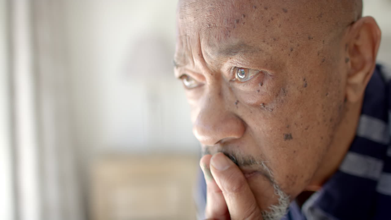 Thoughtful senior biracial man looking through window in bedroom, slow motion