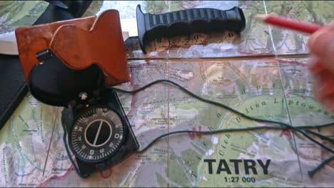 hitchiker preparing to hike on trail in mountains analyzing the map with a compass, pencil and knife, pov, first perspective