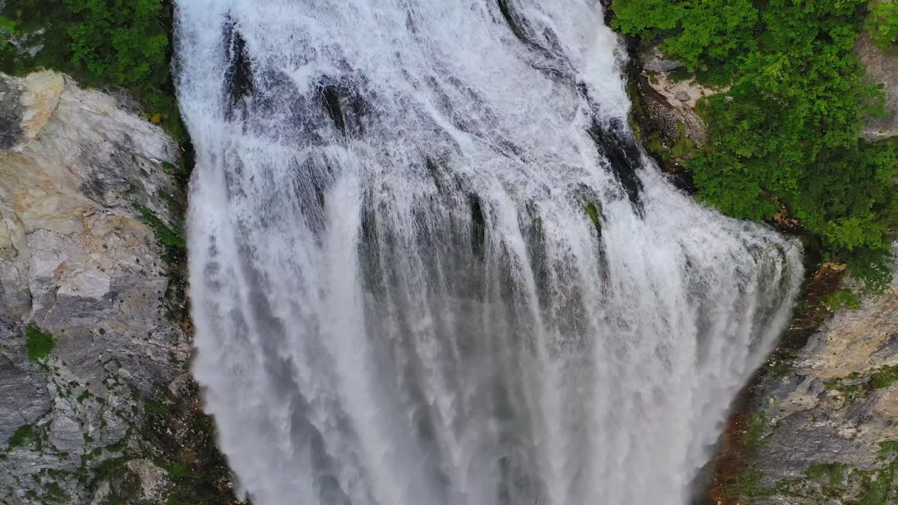 impresionante vista aérea de la majestuosa y poderosa cascada que fluye a través de rocas en medio de empinadas montañas de bosque