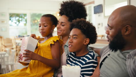 Family-Eating-Popcorn-At-Home-Sitting-On-Sofa-Together-Streaming-Show-Or-Movie-To-TV