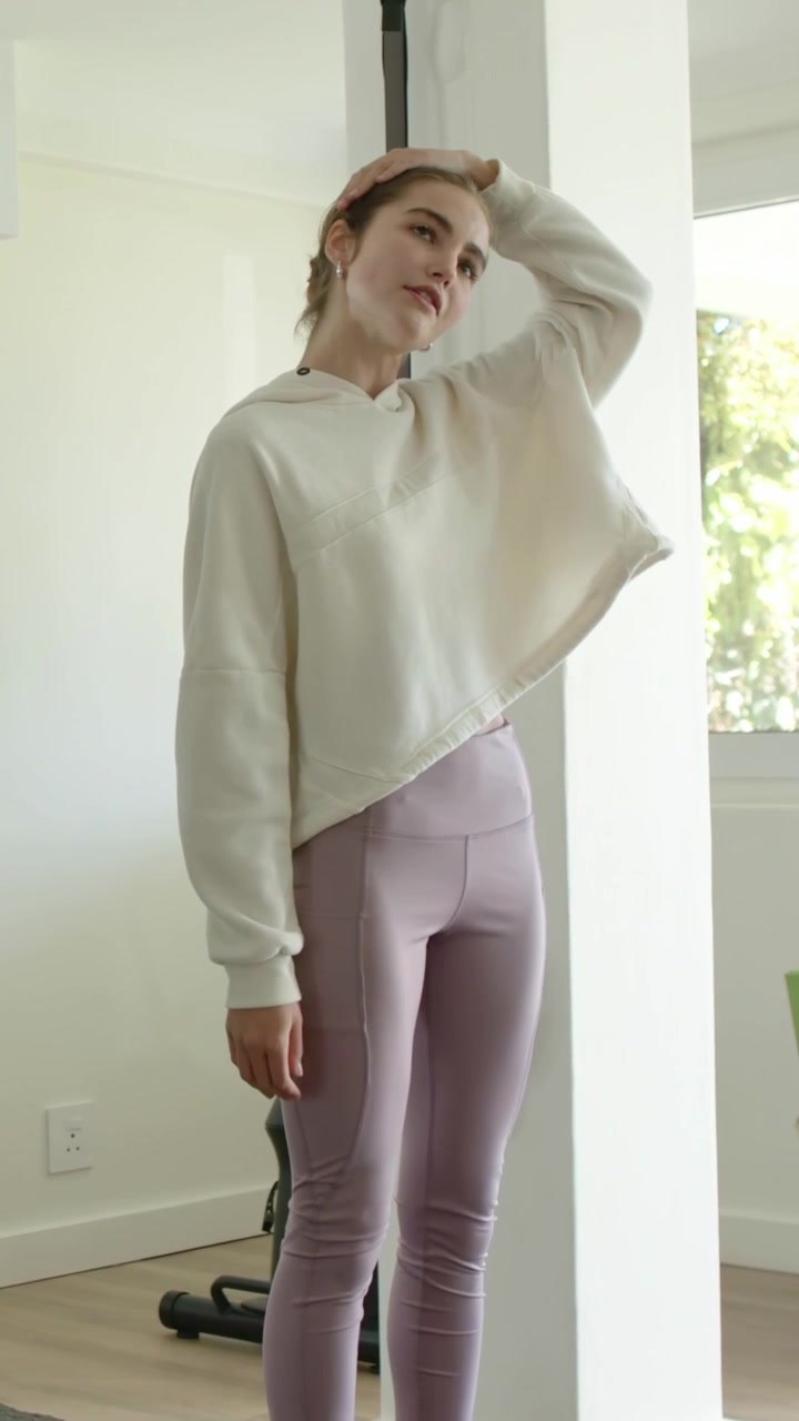 Vertical video: Woman in hoodie shifting doing neck stretch warming up near column with mats in gym