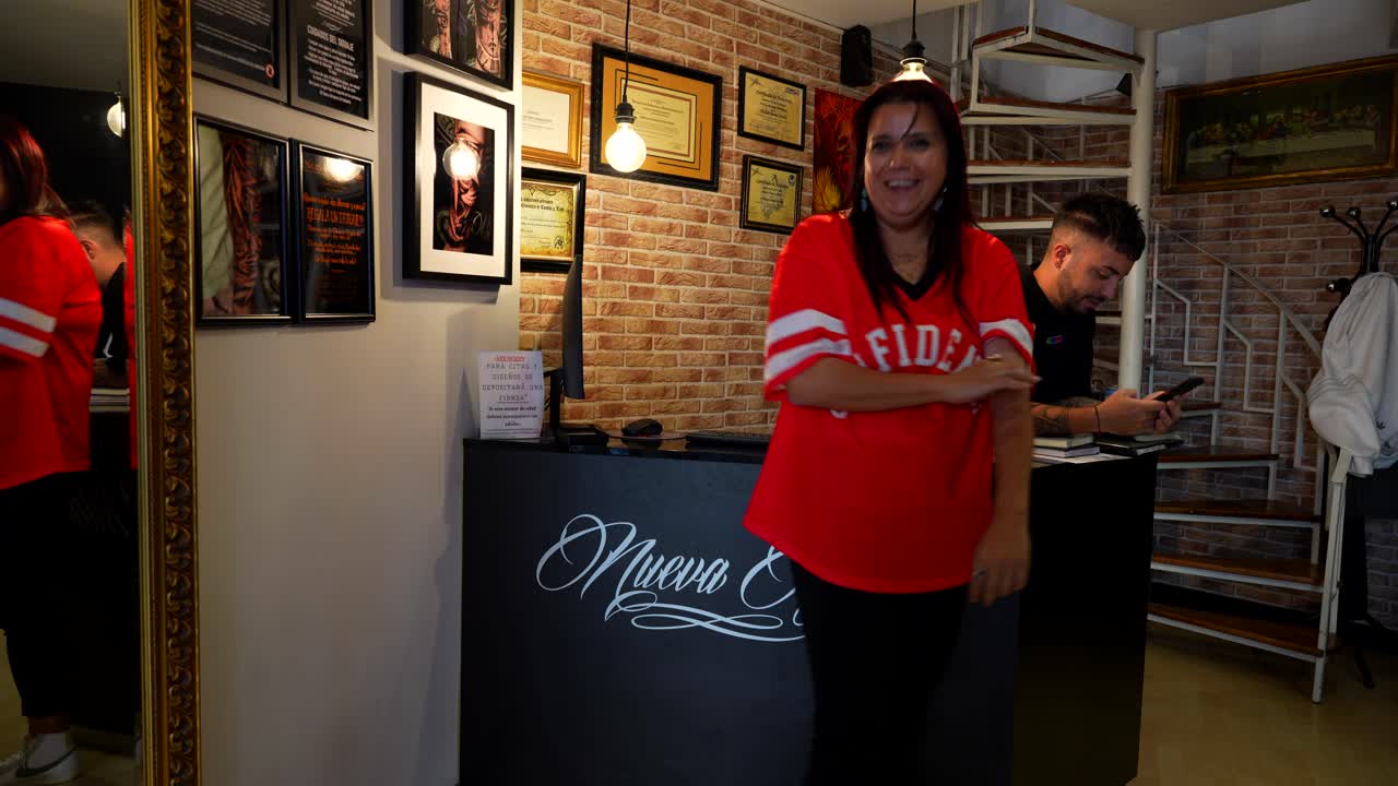 Happy female customer talks with the artist and checks the recent tattoo in a mirror of the studio