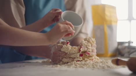 woman is kneading dough on kitchen table and her child is helping little girl is pouring water closeup view