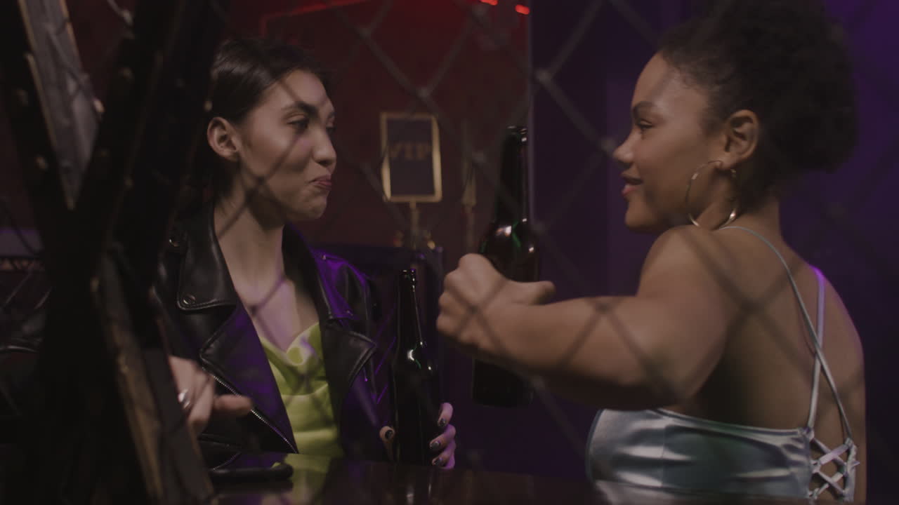 Two Multiethnic Girls Drinking Beer And Talking To Each Other At Disco 2