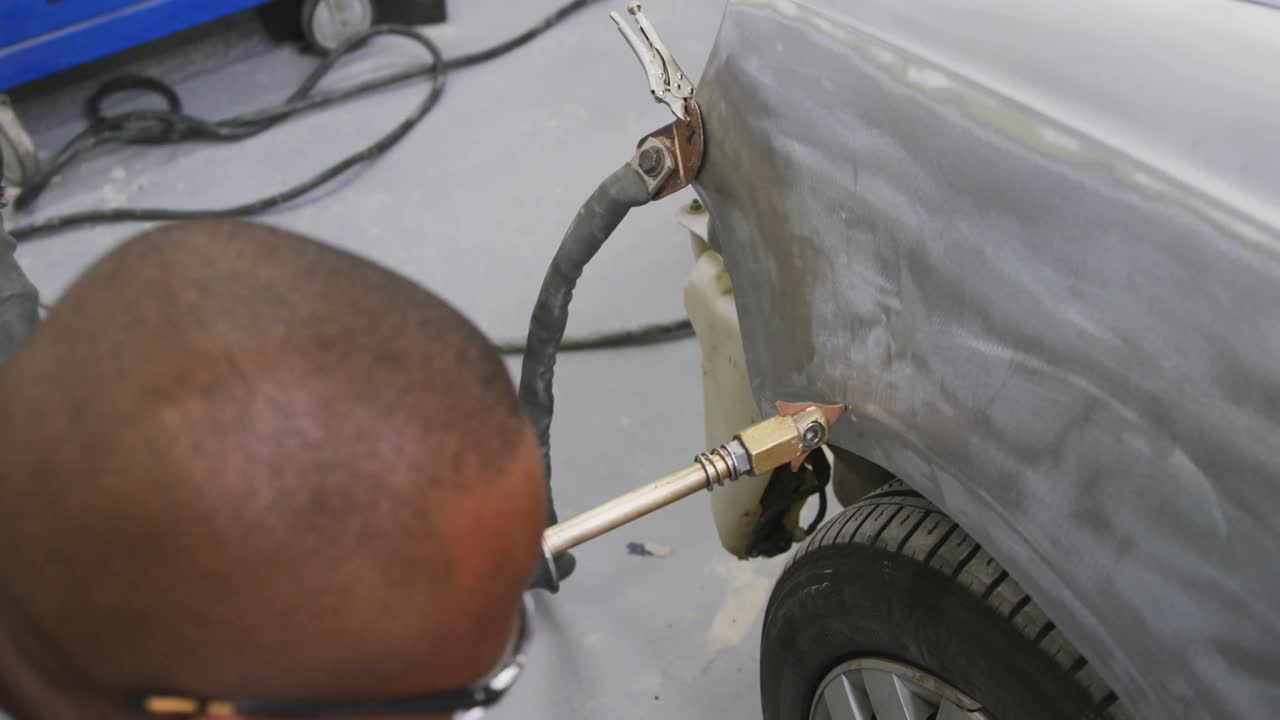 mecánico de automóviles afroamericano que sostiene un destornillador y frota el costado de un automóvil