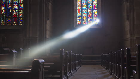 sunlight streams through a stained glass window in a dark church