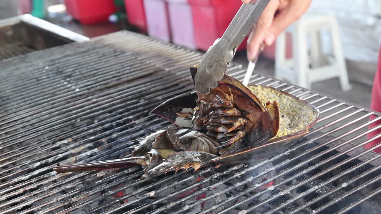 Close-up of shellfish being expertly grilled with tongs over an outdoor metal grill.