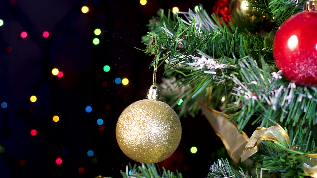 poniendo un ornamento de oro brillante en el árbol de navidad con luces de colores parpadeantes