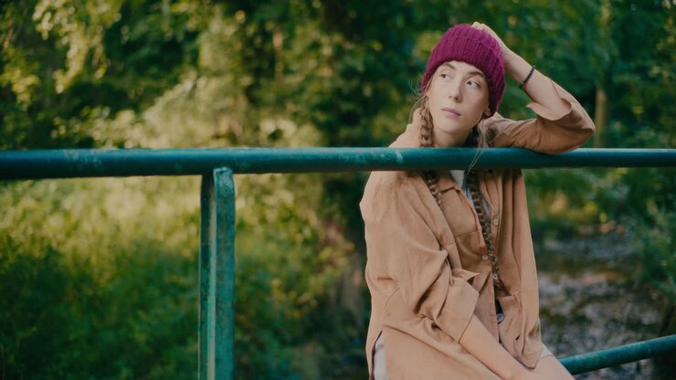 Donna con cappello di lana seduta su una ringhiera nella foresta