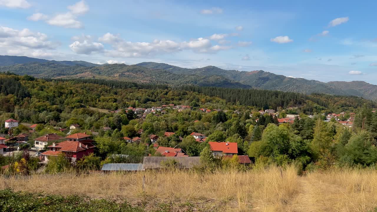 Panning shot of the town of Apriltsi from above against the backdrop of Stara Planina mountain. Red tiled roofs on houses. Panorama shot of Apriltsi. Scenic view