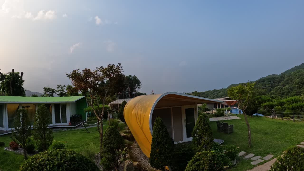 A beautiful sunset timelapse showing the changing sky and golden hour light over unique, modern cabins at a peaceful glamping resort nestled in the mountains of Gapyeong, South Korea