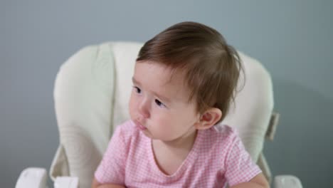 Cute,-grumpy-baby-in-a-highchair-refuses-to-eat-her-oatmeal-cereal-and-makes-whiny-protesting-and-unhappy-gestures-of-complaint