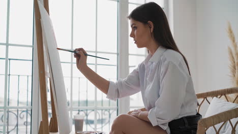 young woman draws painting sitting on chair in art studio