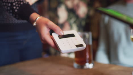 close up of customer paying bill in bar using mobile payment on phone with contactless card reader