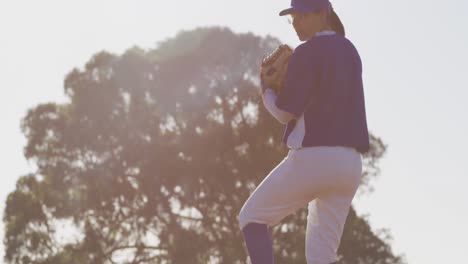 caucasian female baseball player wearing glasses pitching ball on sunny baseball field