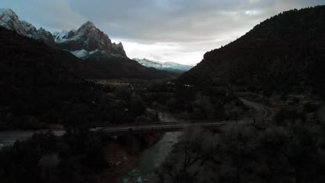 drone shot of a stunning mountain ridge during sunset with snow on the peak of the mountains and a winding road between them.
