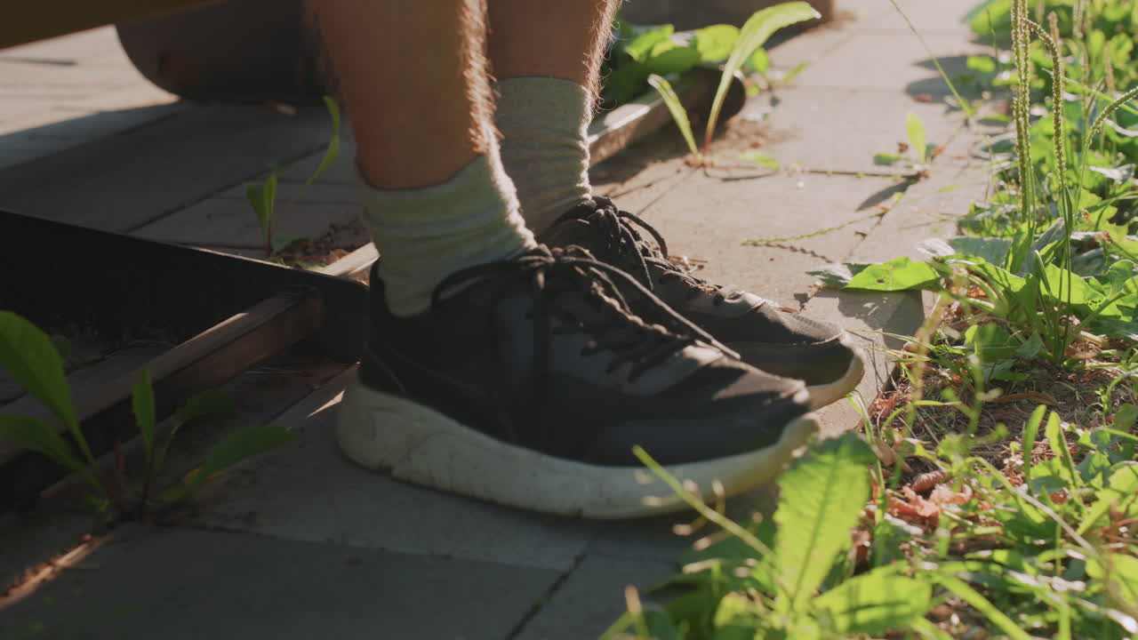 While Warm Sunlight Bathes Surroundings, Feet Settle Close To Aged Railway Ties, Foot Rests By Weathered Rail And Calm Weeds, Lone Foot Rests Near Rusted Railway And Gentle Sunlit Weeds