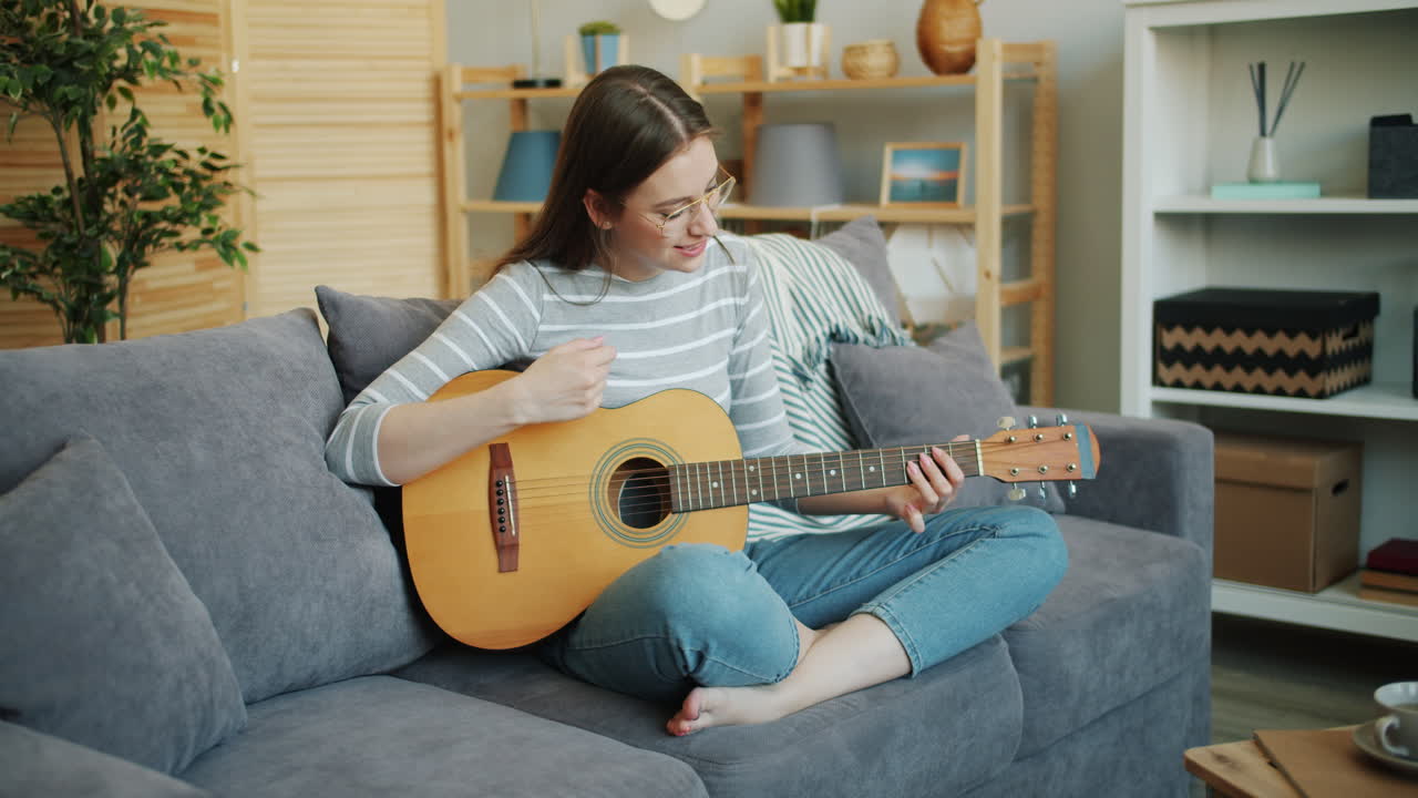 женщина играет на акустической гитаре на диване