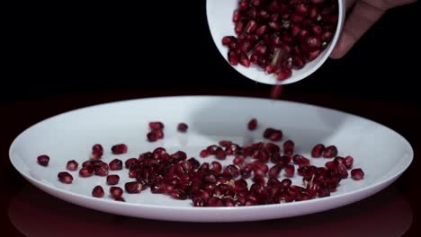 pomegranate seeds falling on white plate from the pot, juicy grains of red ripe