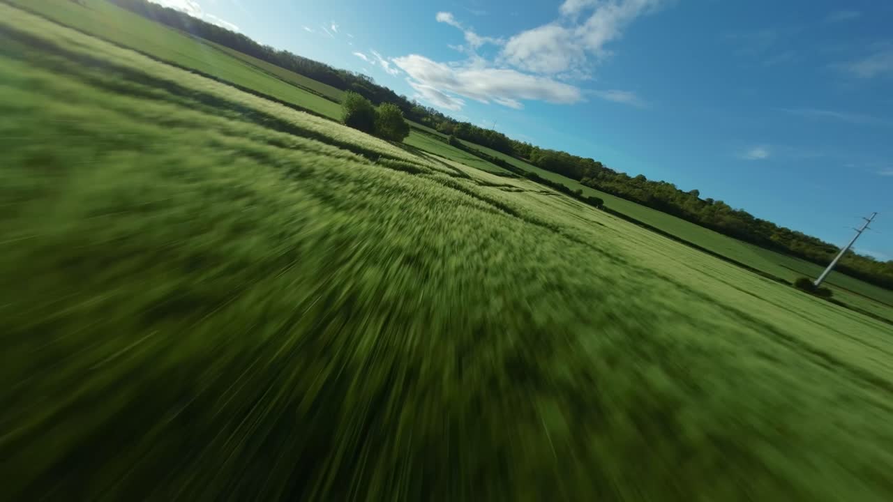 FPV drone breathtaking speed flight above lush green crop fields, motion with scenic landscapes and trees in background under clear blue sky in Montois, France.