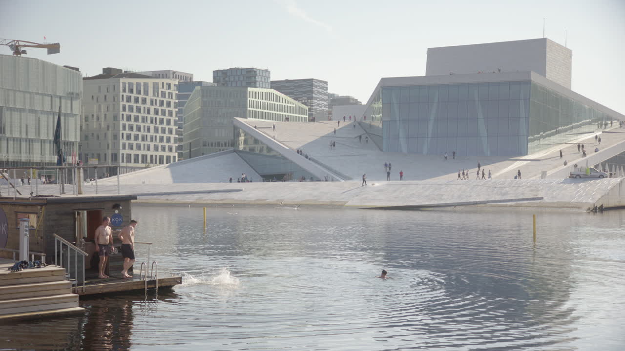 A man dives in from a floating sauna in front of the Opera House, Oslo, slomo