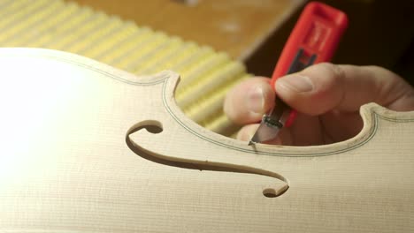 macro-close-up-of-artisan-luthier-maker-work-on-new-classic-handmade-raw-violin-smooth-edge-in-waist-and-purfling-rasp-in-workbench-of-workshop-in-Cremona-Italy-4k-video