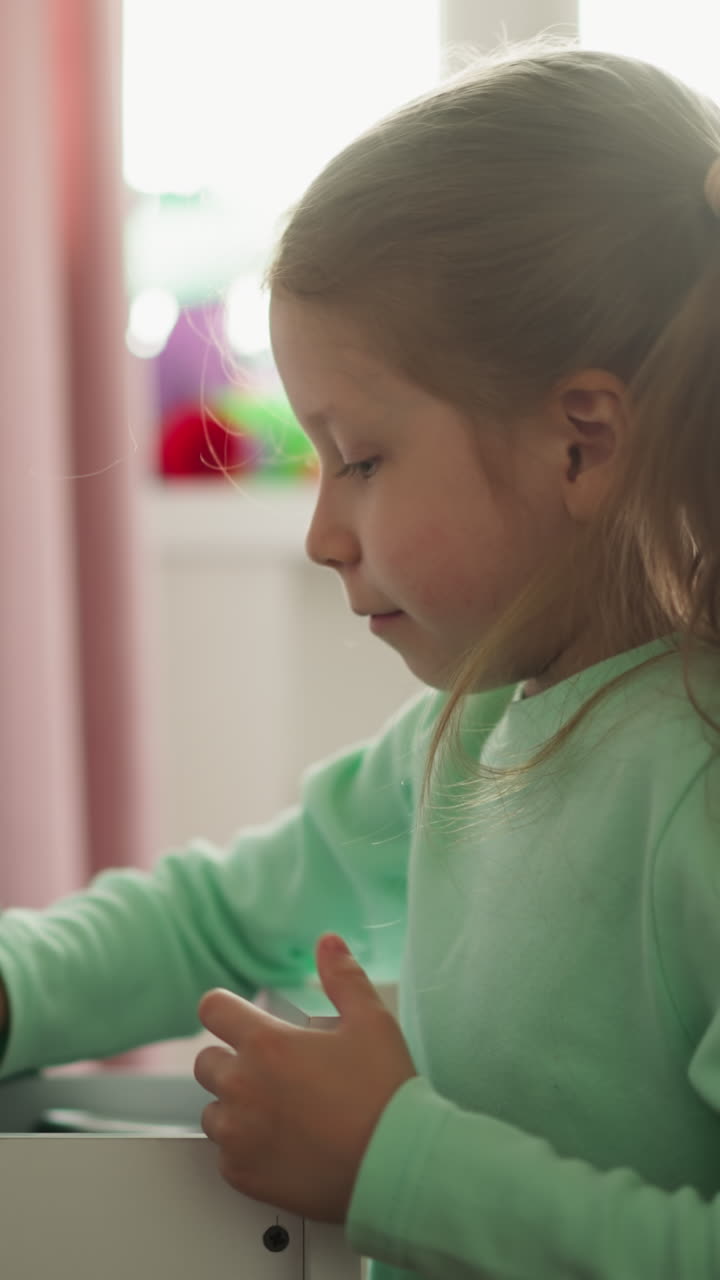 Happy girl finds new color markers pack under folder in desk drawer in children room. Smiling child seeks tool for drawing at home. Schoolgirl and table box