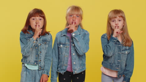 three girls siblings friends presses finger to lips makes silence gesture sign do not tells secret