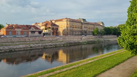 serene spring evening view over the nišava river, with the banovina university building reflected in the calm, clear water under soft sunlight in niš, serbia
