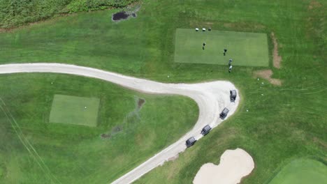 overhead view from a drone looking at a green golf course and groups of golfers walking to their carts.