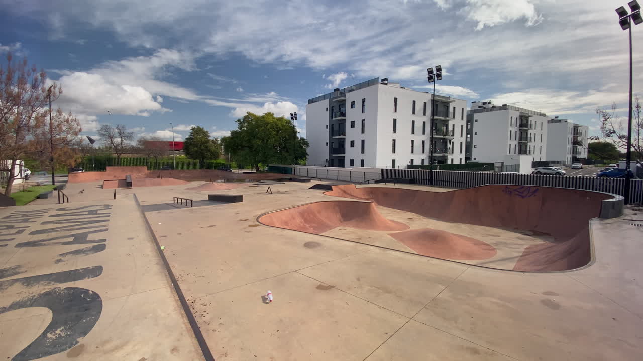 Skatepark exterior vacío en un día soleado, con modernos edificios residenciales blancos y árboles al fondo