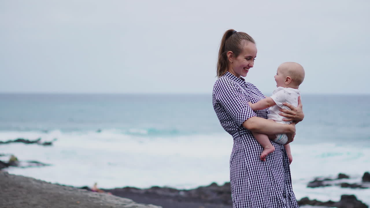 el sonido de las olas acompaña a la madre mientras juega lanzando a su hijo en el aire en la orilla del mar. una joven familia comparte momentos alegres junto al mar
