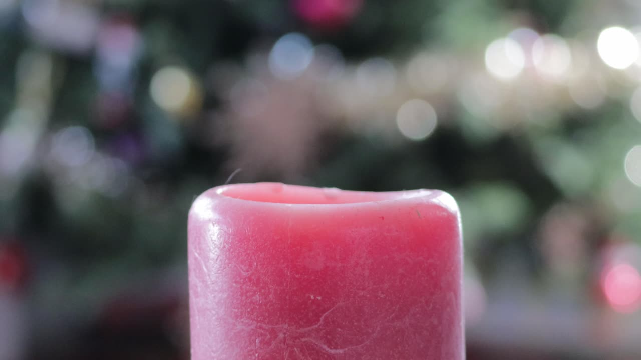 Una candela natalizia accesa da destra di fronte a un albero di Natale, con fumo che esce e si disperde dalla fiamma