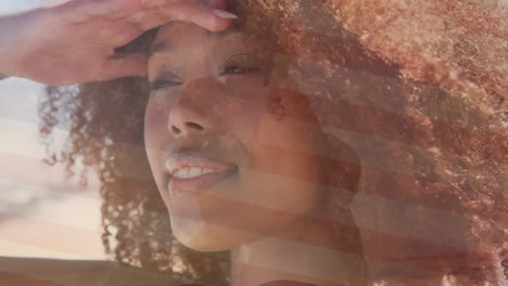 Animation-of-flag-of-united-states-of-america-over-happy-african-american-woman-on-beach