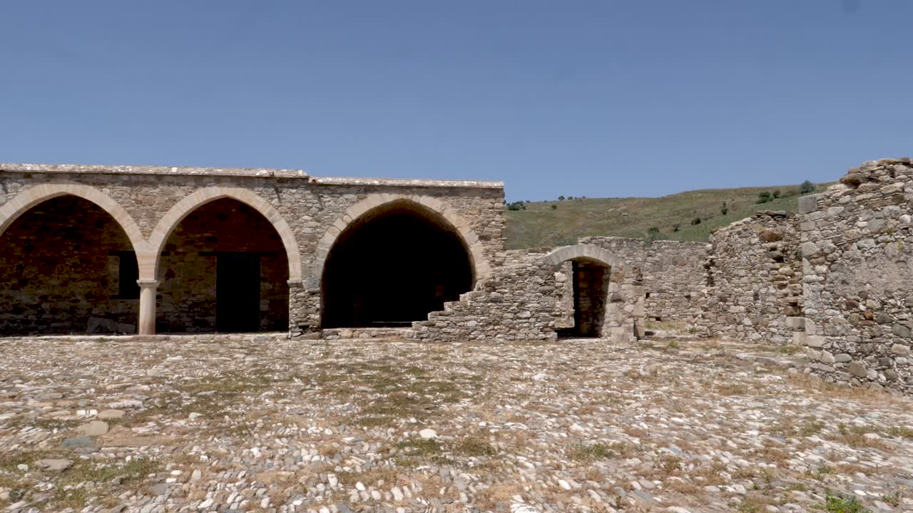 Discover the beauty of historic ruins featuring stone arches under a clear blue sky. This serene location showcases ancient architecture surrounded by rolling hills