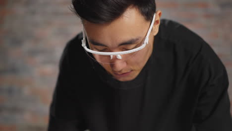 man with face shield looks down against blurry brick wall