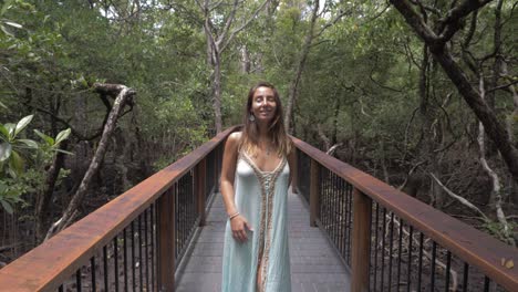 una mujer encantadora con un vestido seductor mira hacia arriba mientras está de pie en el puente en la selva tropical de daintree en el norte de queensland, australia