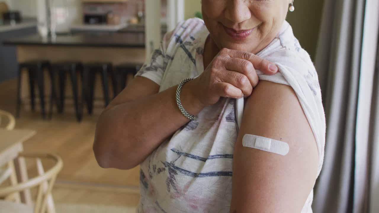 Happy mixed race senior woman showing plaster on arm after covid vaccination