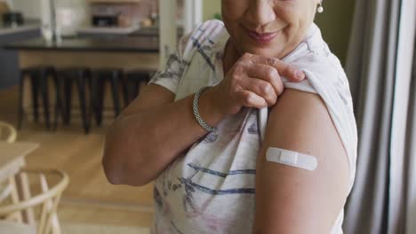 happy mixed race senior woman showing plaster on arm after covid vaccination