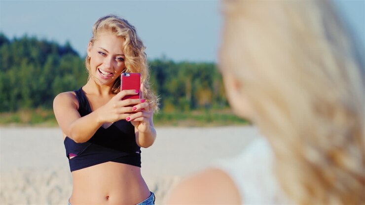 Ung attraktiv kvinde med en smartphone tager billeder af sin kæreste på stranden.