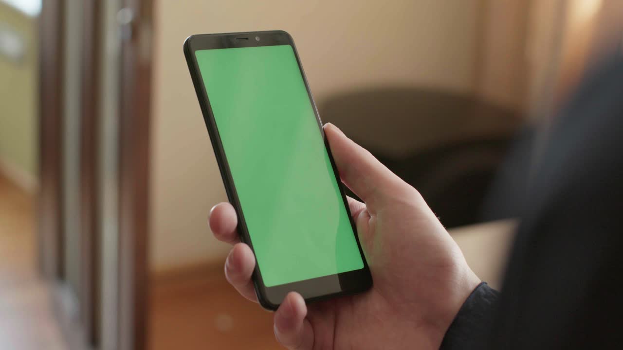 Person holding a smartphone with a green screen