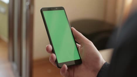 person holding a smartphone with a green screen