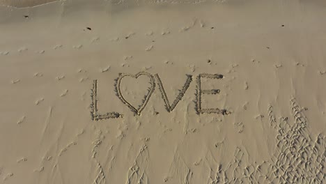 love inscribed in the sand on a beach and it growing in size