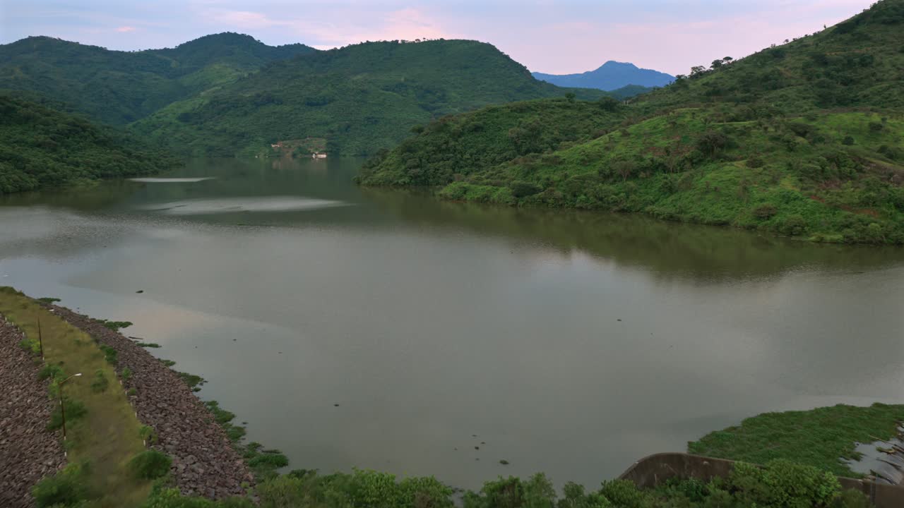 Drone video captures the serene Presa EL Carrizo, nestled among Jalisco's lush hills. The tranquil dusk light enhances the expansive landscape's calm ambiance