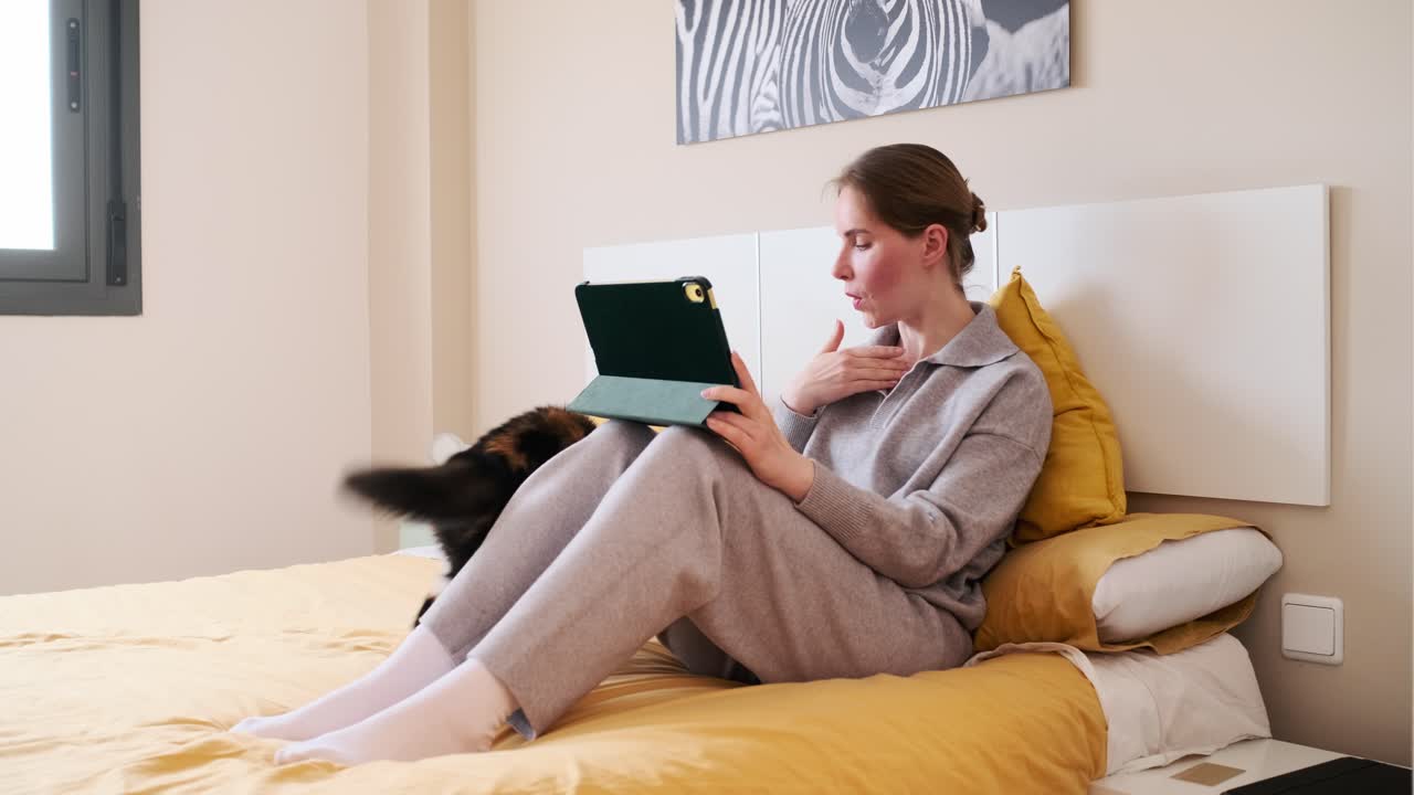 Woman on bed with tablet and cat