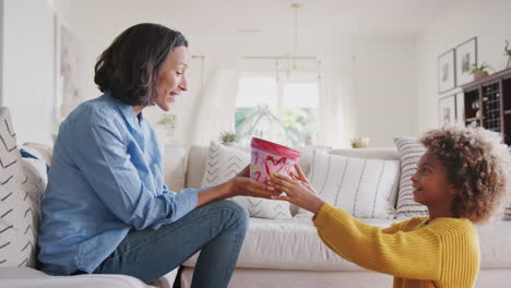 Pre-teen-African-American-girl-giving-her-mum-a-homemade-painted-plant-pot-as-a-gift,-side-view