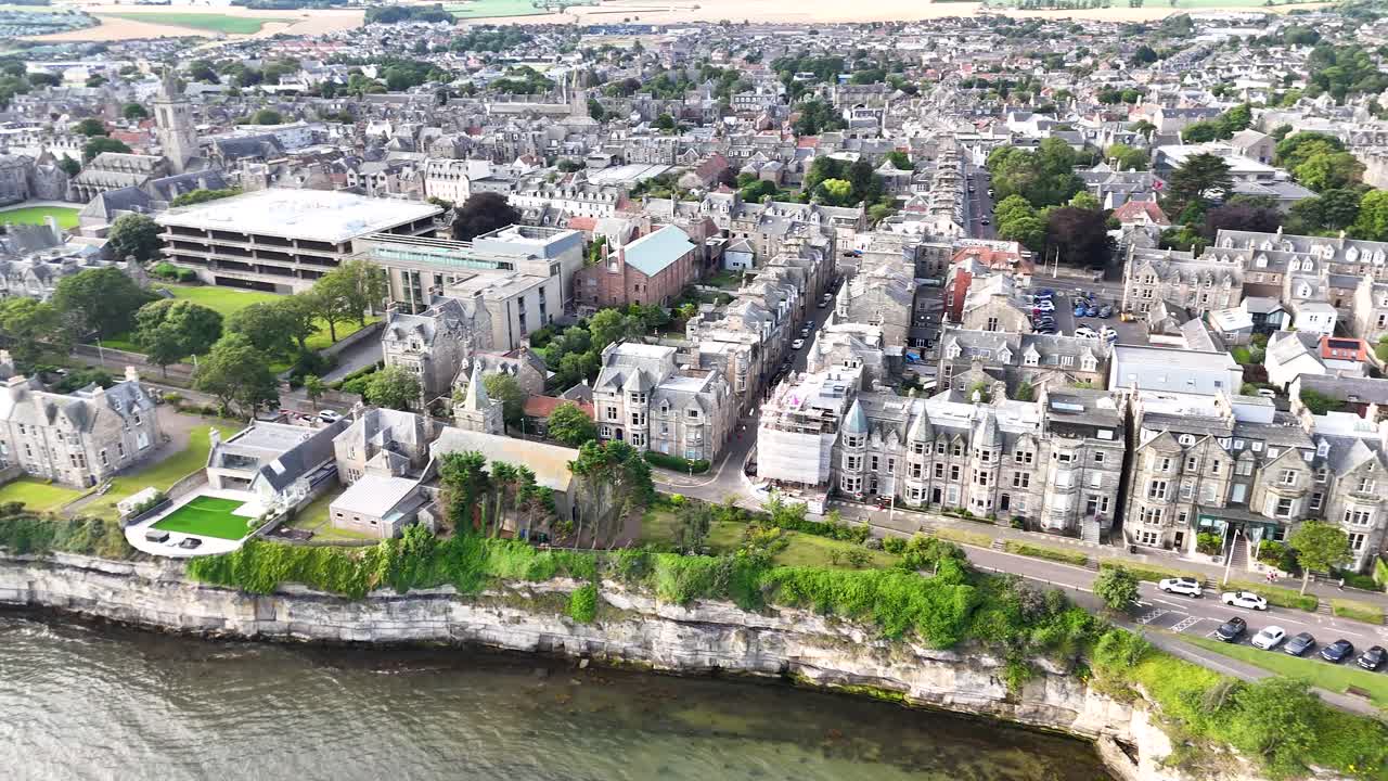 High-resolution aerial footage glides above St Andrews, Scotland, revealing historic stone buildings, dramatic cliffs, and waterfront under bright natural daylight