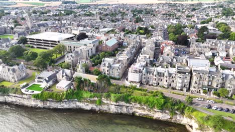 high-resolution aerial footage glides above st andrews, scotland, revealing historic stone buildings, dramatic cliffs, and waterfront under bright natural daylight