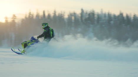 snowmobile rider leaving snowy powder trail speeding across arctic circle woodland at sunrise